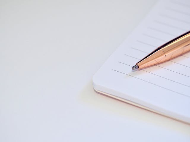 Różowozłoty długopis położony na zeszycie w linie ponowne ujęcie